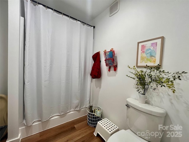 bathroom with hardwood / wood-style flooring, shower / bath combination with curtain, and toilet