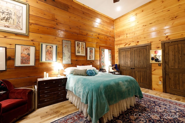 bedroom with wood walls, a towering ceiling, and light hardwood / wood-style flooring