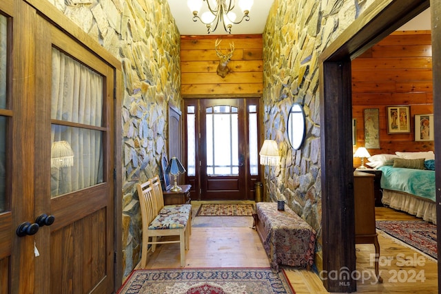 entrance foyer with wooden walls, a chandelier, and light wood-type flooring