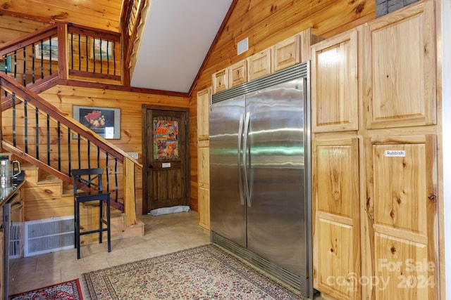 kitchen featuring light brown cabinetry, stainless steel built in refrigerator, vaulted ceiling, wooden walls, and light tile patterned floors