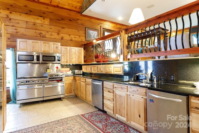 kitchen featuring appliances with stainless steel finishes, light brown cabinets, wood walls, and sink