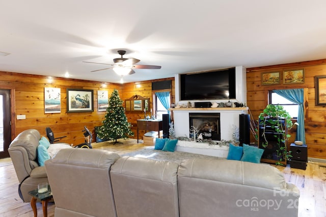 living room with ceiling fan, light wood-type flooring, and wooden walls