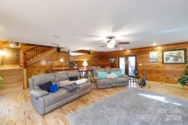 living room with ceiling fan, wood walls, light wood-type flooring, and french doors