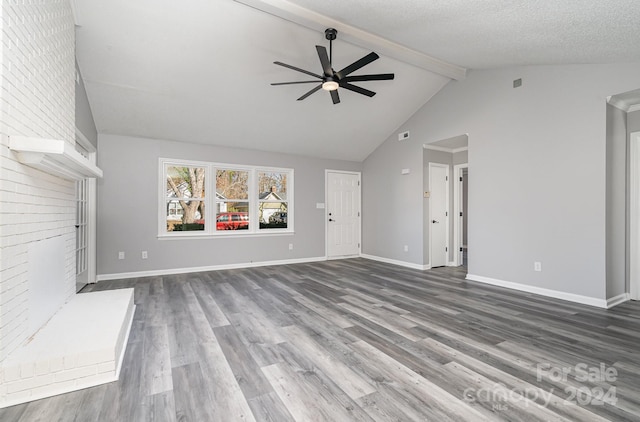 unfurnished living room with a brick fireplace, a textured ceiling, ceiling fan, vaulted ceiling with beams, and dark hardwood / wood-style floors