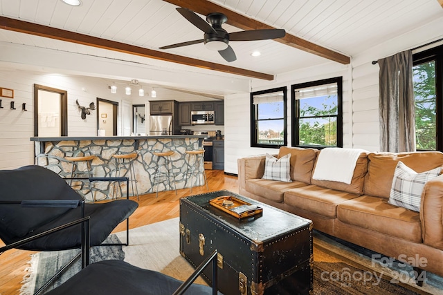 living room with wooden walls, light hardwood / wood-style flooring, ceiling fan, beamed ceiling, and wood ceiling