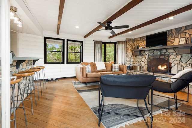 living room with beam ceiling, a stone fireplace, a wealth of natural light, and wood-type flooring