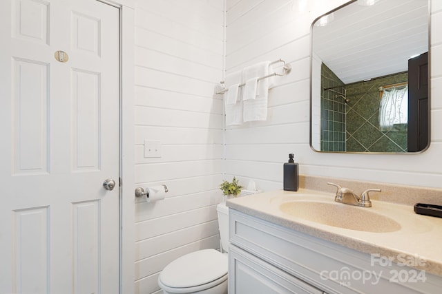 bathroom with tiled shower, wooden walls, vanity, and toilet