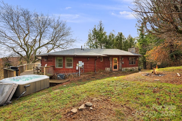 rear view of house with a hot tub, a lawn, and a wooden deck