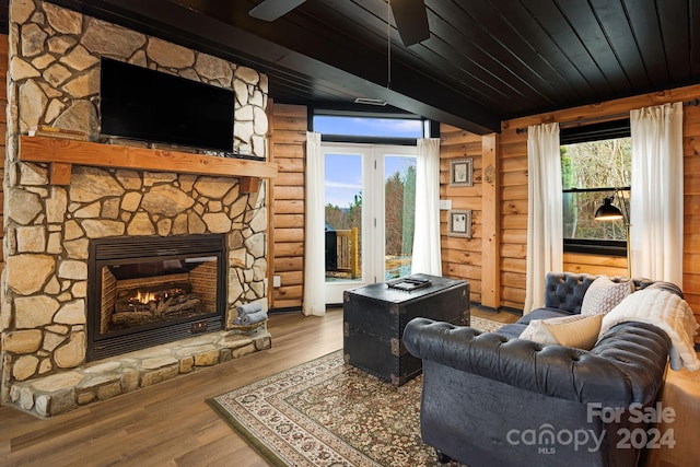 living room featuring rustic walls, ceiling fan, wooden ceiling, hardwood / wood-style floors, and a stone fireplace