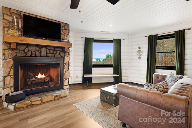 living room with a stone fireplace, a wealth of natural light, wooden ceiling, and light wood-type flooring