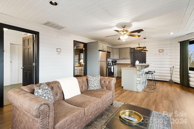 living room with ceiling fan, wooden walls, wooden ceiling, and light wood-type flooring