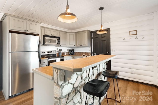 kitchen featuring wood-type flooring, stainless steel appliances, decorative light fixtures, and a kitchen breakfast bar