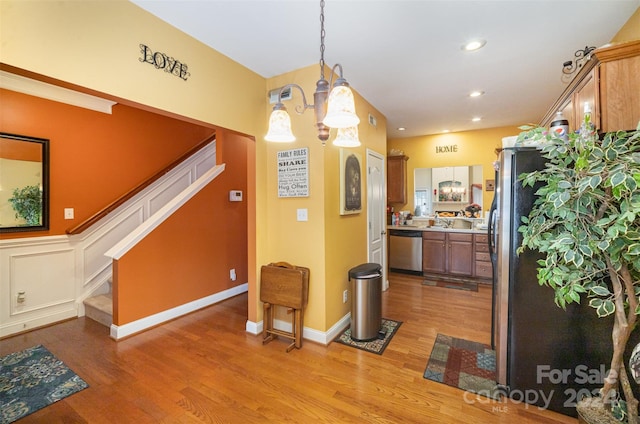 kitchen featuring appliances with stainless steel finishes, light wood-type flooring, sink, pendant lighting, and a notable chandelier