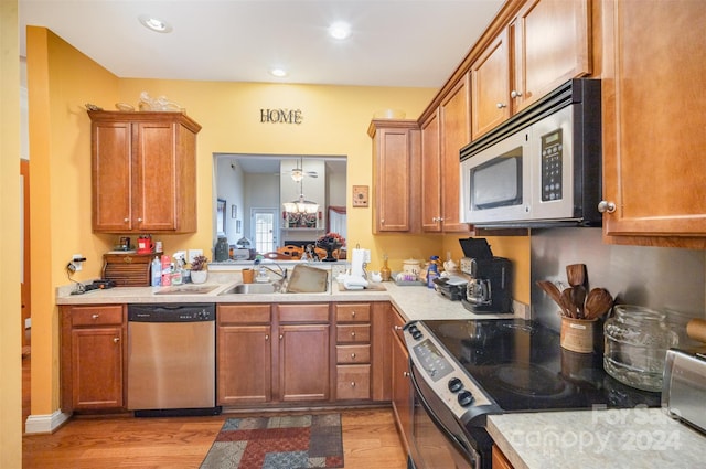 kitchen featuring sink, light hardwood / wood-style flooring, pendant lighting, a chandelier, and appliances with stainless steel finishes