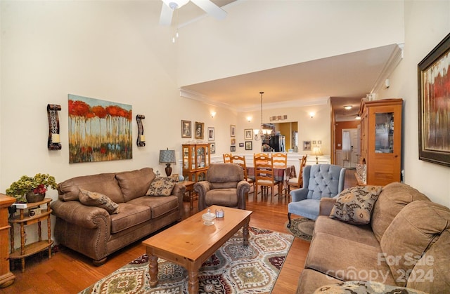 living room with hardwood / wood-style floors, ceiling fan with notable chandelier, ornamental molding, and a high ceiling