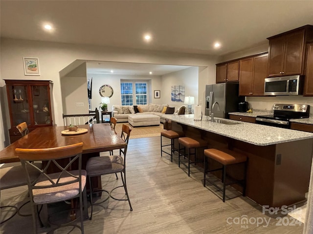 kitchen with dark brown cabinetry, stainless steel appliances, a kitchen island with sink, sink, and light hardwood / wood-style floors