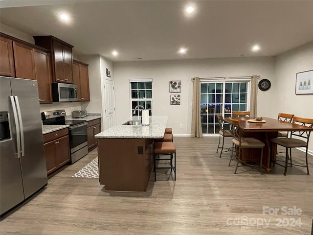 kitchen with light stone countertops, sink, stainless steel appliances, light hardwood / wood-style floors, and a center island with sink