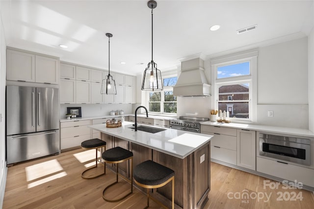 kitchen featuring a kitchen island with sink, sink, light hardwood / wood-style flooring, custom range hood, and stainless steel appliances