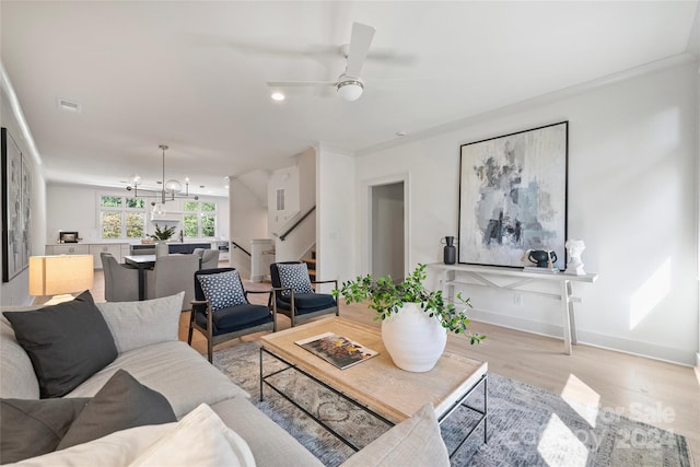 living room featuring ornamental molding, ceiling fan with notable chandelier, and light wood-type flooring