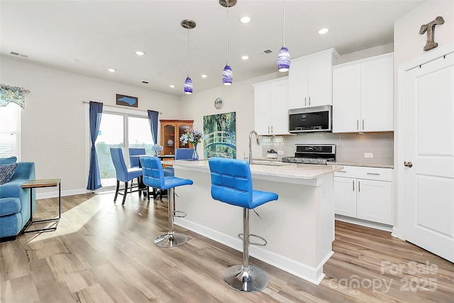 kitchen featuring a breakfast bar, stainless steel appliances, white cabinets, a center island with sink, and decorative light fixtures