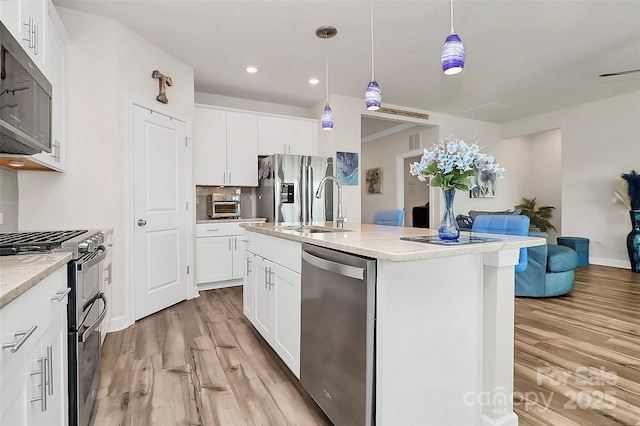 kitchen with stainless steel appliances, decorative light fixtures, an island with sink, and white cabinets