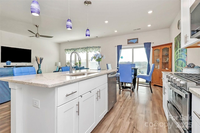 kitchen with sink, a kitchen island with sink, hanging light fixtures, stainless steel appliances, and white cabinets