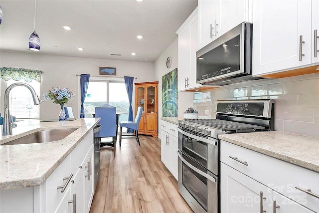 kitchen with sink, white cabinets, backsplash, light stone counters, and stainless steel appliances