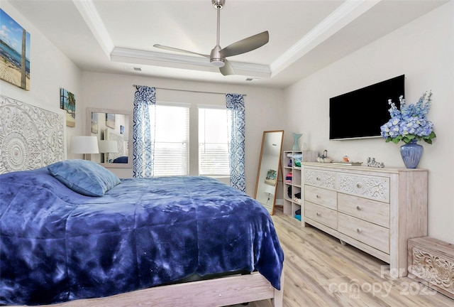 bedroom with ceiling fan, ornamental molding, a tray ceiling, and light wood-type flooring