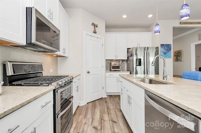 kitchen with appliances with stainless steel finishes, white cabinetry, sink, backsplash, and hanging light fixtures