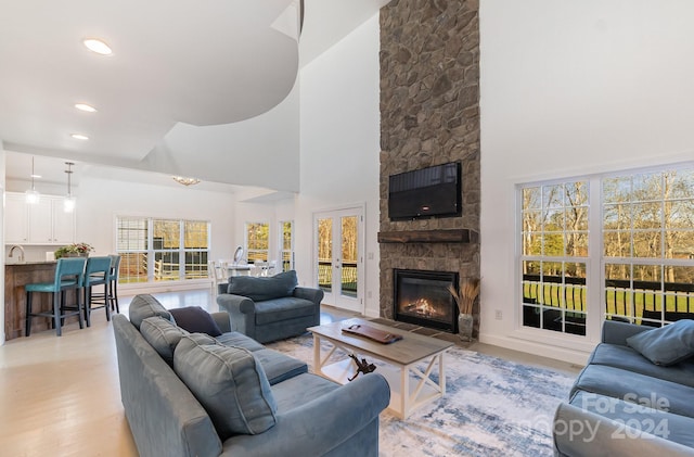 living room with a towering ceiling, light hardwood / wood-style flooring, a stone fireplace, and a healthy amount of sunlight