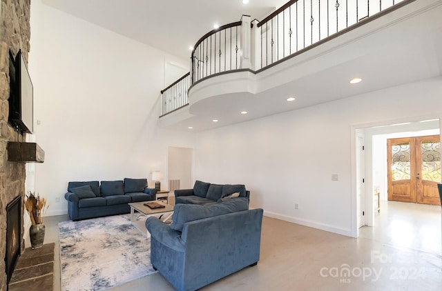 living room featuring concrete flooring, a fireplace, a high ceiling, and french doors