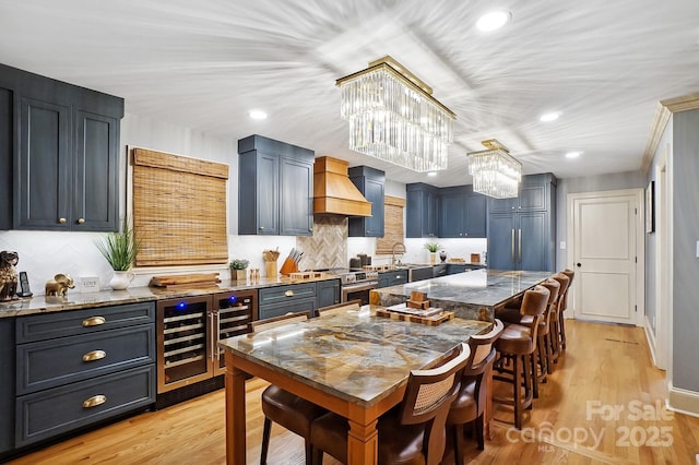 kitchen with beverage cooler, premium range hood, light wood-style floors, stainless steel range with electric cooktop, and dark stone countertops