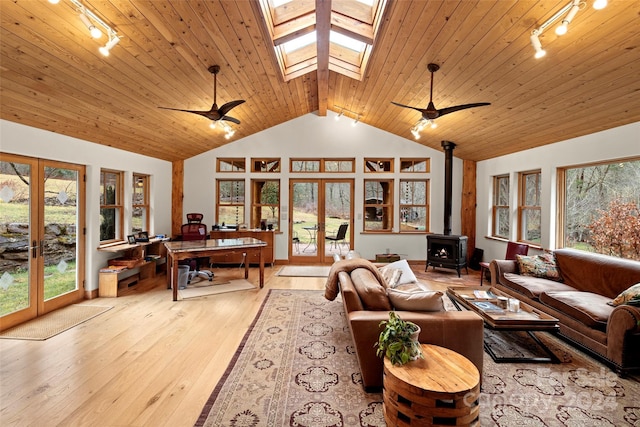 living room with a wood stove, french doors, vaulted ceiling with skylight, and light wood-type flooring