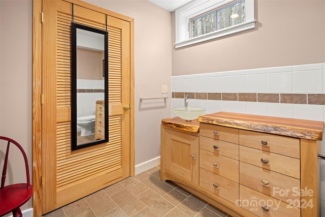 bathroom featuring tile patterned floors, vanity, toilet, and tile walls