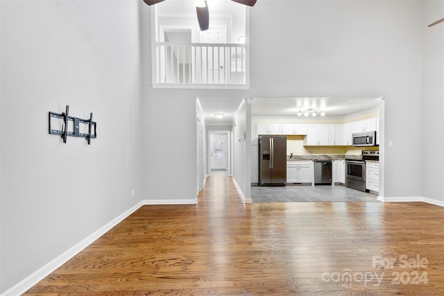 unfurnished living room featuring ceiling fan, light wood-type flooring, sink, and a high ceiling