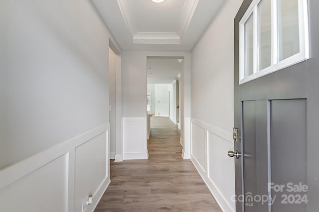 corridor featuring light hardwood / wood-style floors, ornamental molding, and a tray ceiling