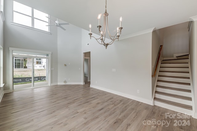 unfurnished living room featuring crown molding, light hardwood / wood-style flooring, a towering ceiling, and ceiling fan with notable chandelier