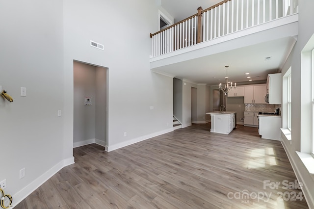 unfurnished living room featuring a notable chandelier, light hardwood / wood-style floors, sink, and a high ceiling