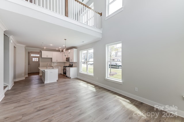 kitchen with stainless steel appliances, light hardwood / wood-style floors, decorative light fixtures, a center island with sink, and white cabinets