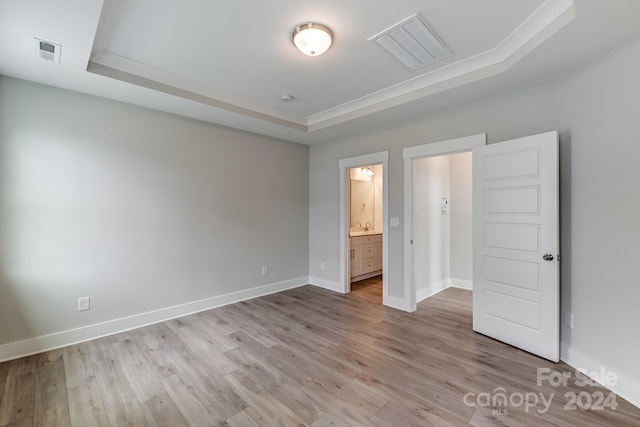 unfurnished bedroom featuring a tray ceiling, ensuite bath, light hardwood / wood-style floors, and sink