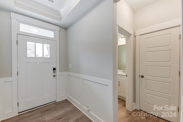 foyer featuring a raised ceiling, sink, and light wood-type flooring