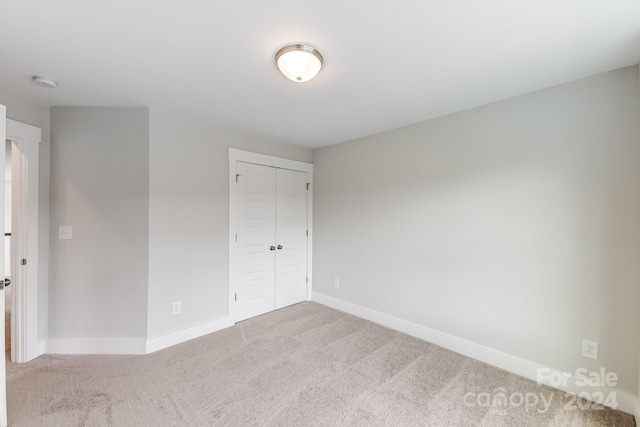 unfurnished bedroom with light colored carpet and a closet