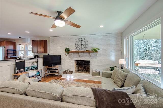 living room featuring a brick fireplace, brick wall, ceiling fan, sink, and hardwood / wood-style floors