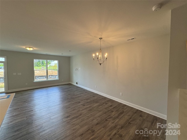 spare room with an inviting chandelier and dark wood-type flooring