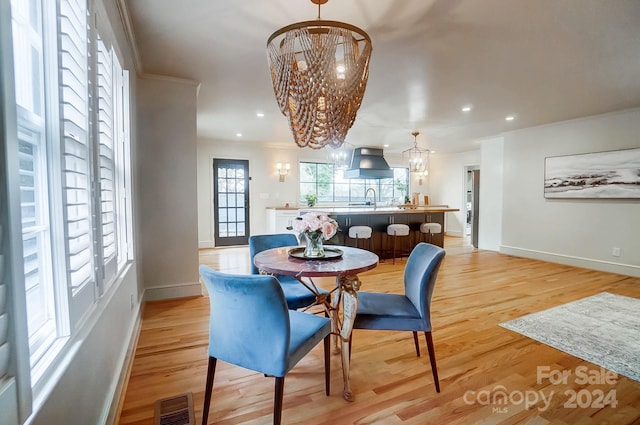 dining room with sink, light hardwood / wood-style flooring, a notable chandelier, and ornamental molding