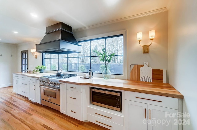 kitchen with appliances with stainless steel finishes, custom range hood, light hardwood / wood-style flooring, white cabinets, and butcher block counters