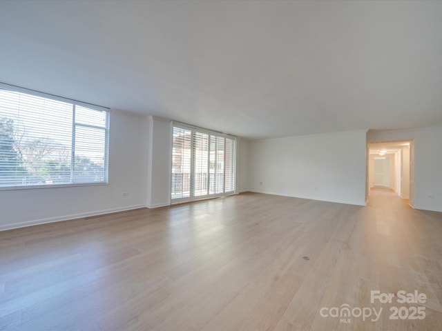 empty room with plenty of natural light, light wood-style flooring, and baseboards