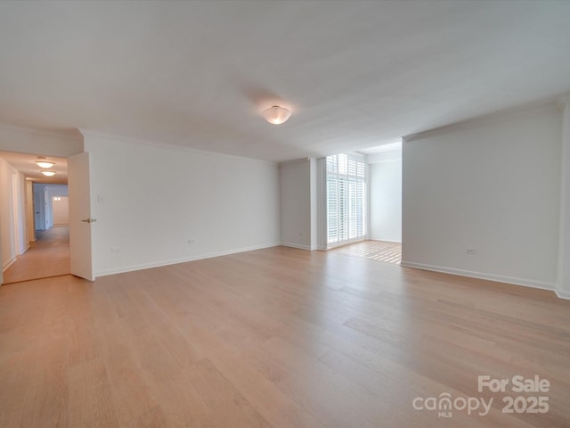 empty room featuring ornamental molding, light wood-type flooring, and baseboards