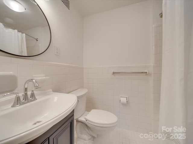 bathroom with a wainscoted wall, tile walls, toilet, and vanity