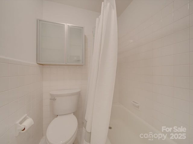 bathroom with toilet, a shower with curtain, and tile walls